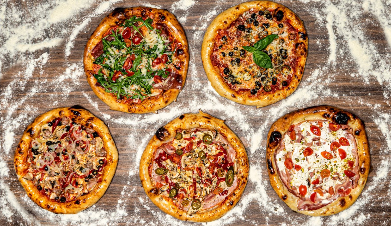 Penkios šviežiai keptos Toni Pizza picos ant miltuoto medinio paviršiaus